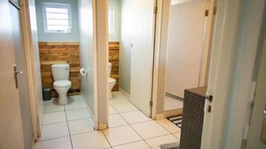 A narrow hallway with two toilets, one with a wooden wall and the other with a plain wall.