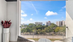 Varanda com móveis de vime, planta em vaso e vista para edifícios e árvores.
