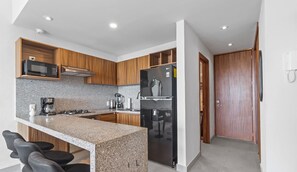 Cozinha moderna com bancadas de granito, micro-ondas embutido, geladeira de aço inoxidável e armários de madeira.