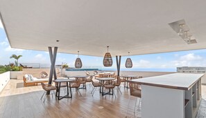 A rooftop terrace with wicker furniture, a bar area, and a view of the sea.