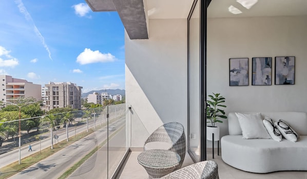 Varanda com vista para a paisagem urbana, um sofá branco e três quadros abstratos.