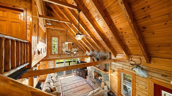 L’intérieur d’un chalet en bois comprend une chambre à coucher située en mezzanine, une cheminée en pierre et des bois de cerf accrochés au mur.
