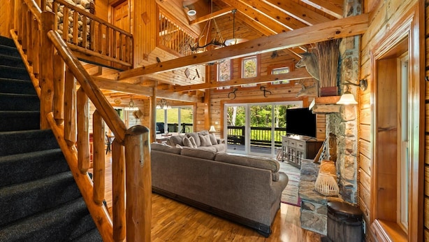L’intérieur d’une cabane en rondins, avec un escalier, un canapé, un téléviseur et une cheminée en pierre.