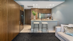 A modern kitchen with wooden cabinets, a central island with stools, a built-in oven, and a large window. - LUXURY LIVING - ICONIC ST KILDA BEACH LOCATION ** ONE MONTH SHORT STAYS **
 (St Kilda)