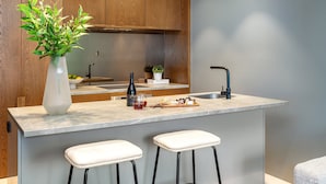 A modern kitchen with wooden cabinets, a marble countertop, a sink, and two bar stools. - LUXURY LIVING - ICONIC ST KILDA BEACH LOCATION ** ONE MONTH SHORT STAYS **
 (St Kilda)