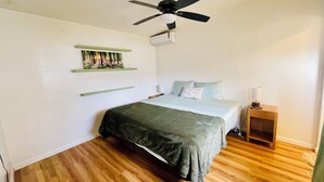 A bedroom with a bed, a ceiling fan, a nightstand, and a wall-mounted air conditioner. - Westside Magic 3bed 2 bath house in terrific westside of oahu!  (Nanakuli)