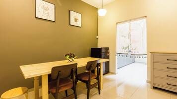 A small dining area with a wooden table and two chairs, a refrigerator, and a cabinet.