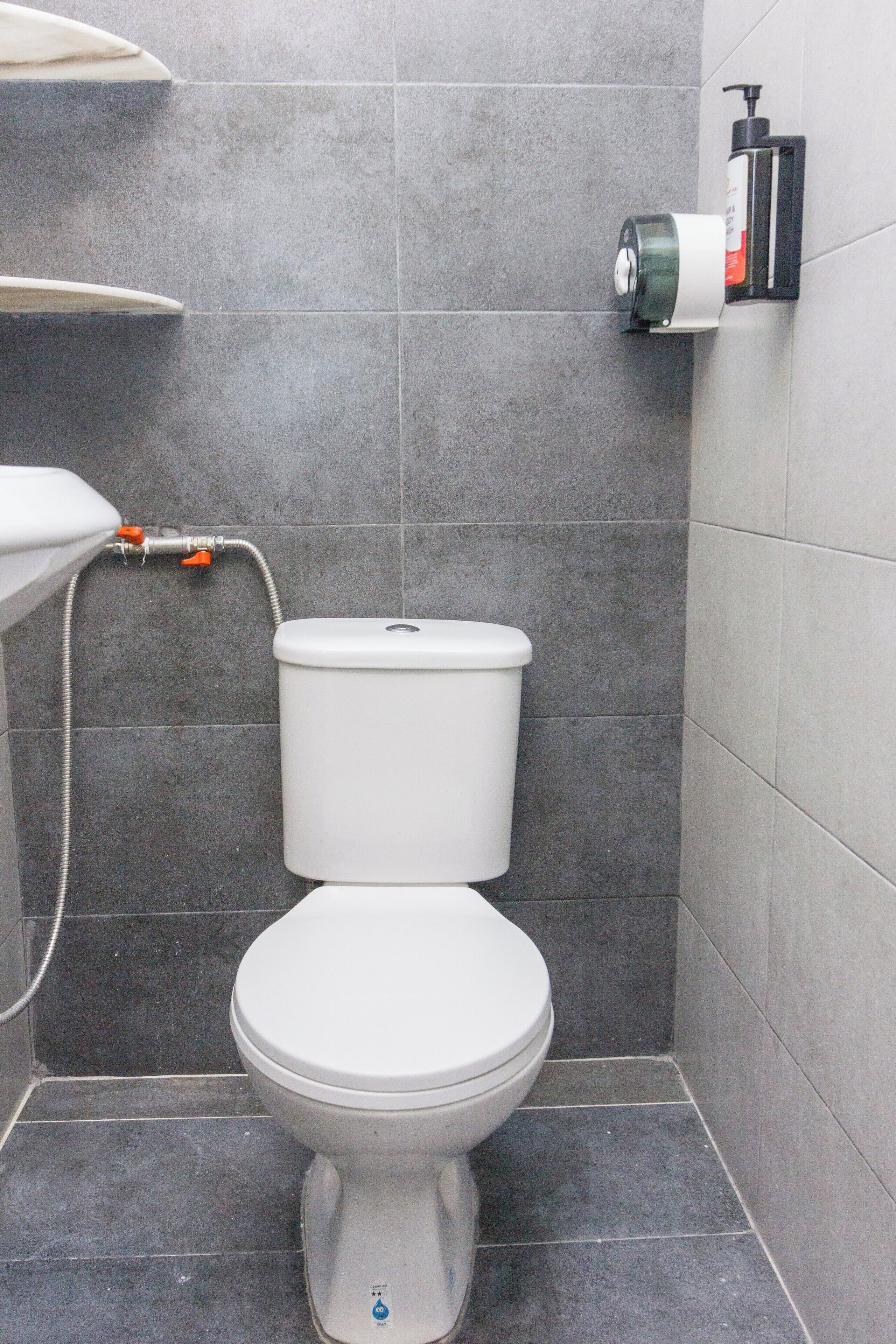 A modern bathroom with a white toilet, a shower, and a hand sanitizer dispenser on the wall.
