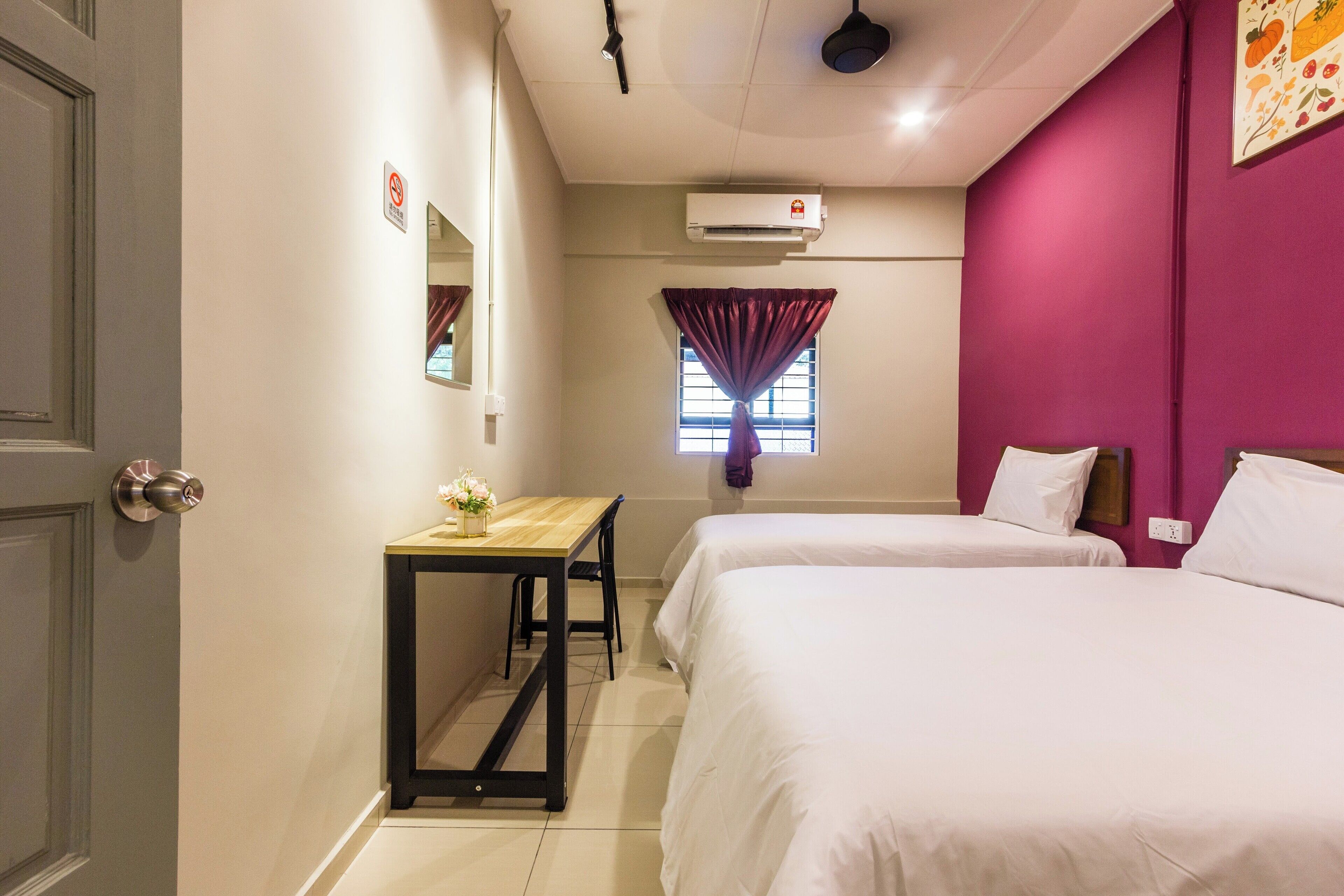 A hotel room with two beds, a desk, a window with curtains, and an air conditioning unit.