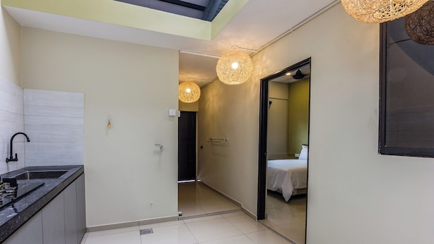 A modern kitchen with a black countertop and a sink, a hallway leading to a bedroom with a bed and a door, and a ceiling with a skylight. - Kimsar 3BR Family Inn by uBook (Perai)