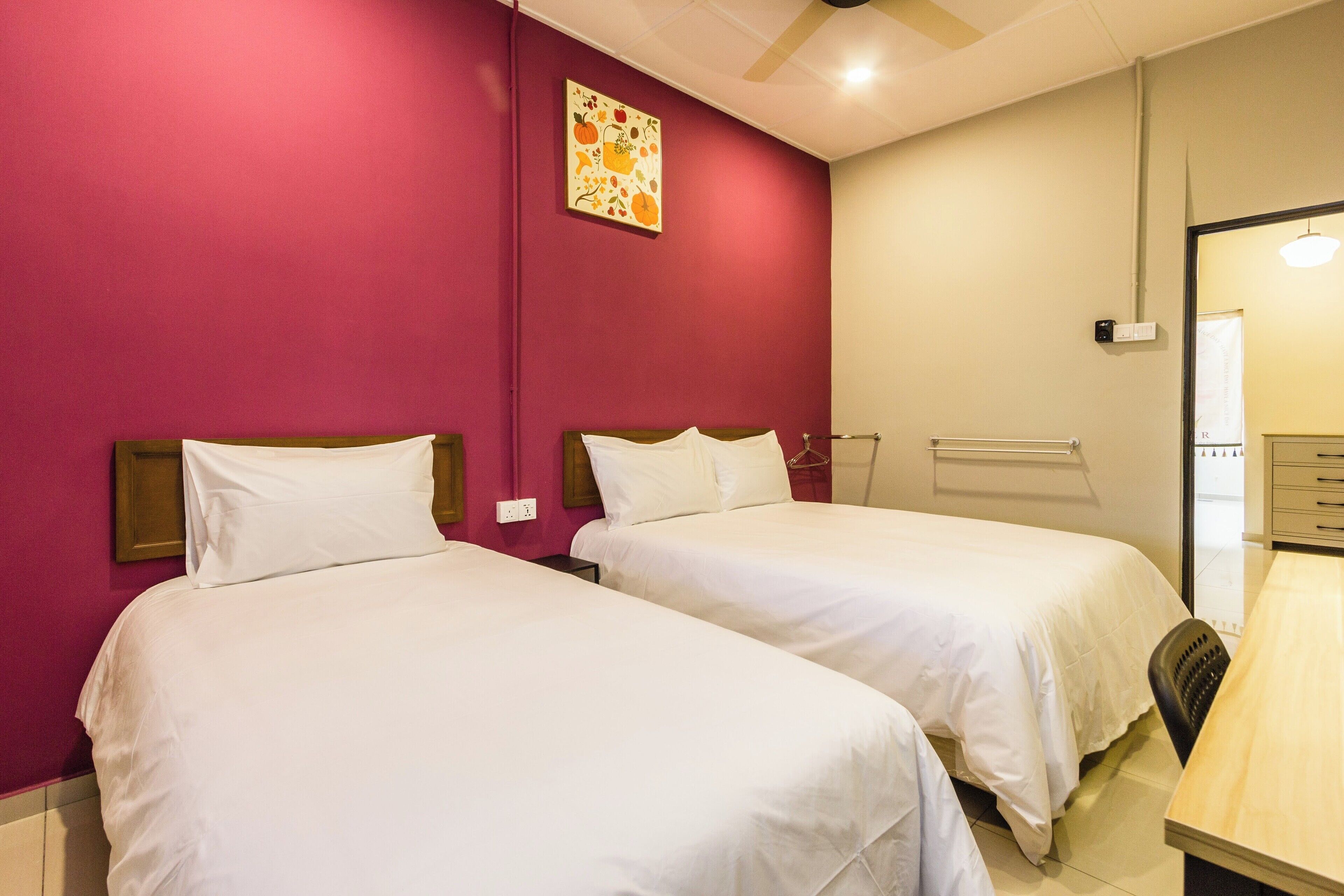 Une chambre d’hôtel avec deux lits, un bureau en bois et un ventilateur de plafond.