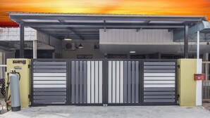 A building with a large metal gate, a covered parking area, and a gas cylinder outside. - Kimsar 3BR Family Inn by uBook (Perai)