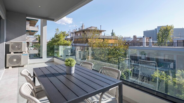 A modern balcony with a dining table and chairs, air conditioning units, and a potted plant. - Prestigious 3BR Apartment in Marousi (Marousi)