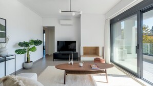 A modern living room with a large TV, a fireplace, and a large window. - Prestigious 3BR Apartment in Marousi (Marousi)