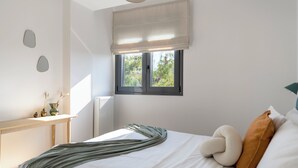 A bedroom with a bed, a window with blinds, a radiator, and a bedside table with a vase. - Prestigious 3BR Apartment in Marousi (Marousi)