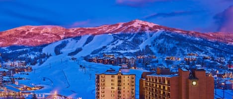 Une montagne enneigée, avec une station de ski en arrière-plan, où l’on aperçoit un grand hôtel à plusieurs étages et un télésiège.