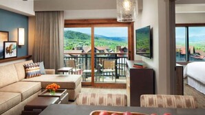 Habitación de hotel con sofá, mesa de comedor con manzanas, televisor y balcón con vistas panorámicas.