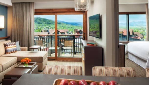 Una habitación de hotel con balcón, zona de comedor y cama.