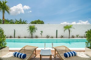 A poolside area with two wicker lounge chairs, a small white table, and a white textured wall. - Baliterraneo Boutique Resort Seminyak (Seminyak)