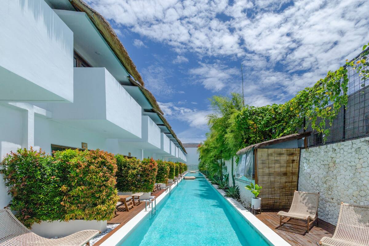 A pool area with a clear blue pool, lounge chairs, and a white building with a thatched roof.