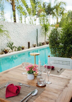 A dining table with a pool view, clear glasses, and a red napkin. - Baliterraneo Boutique Resort Seminyak (Seminyak)