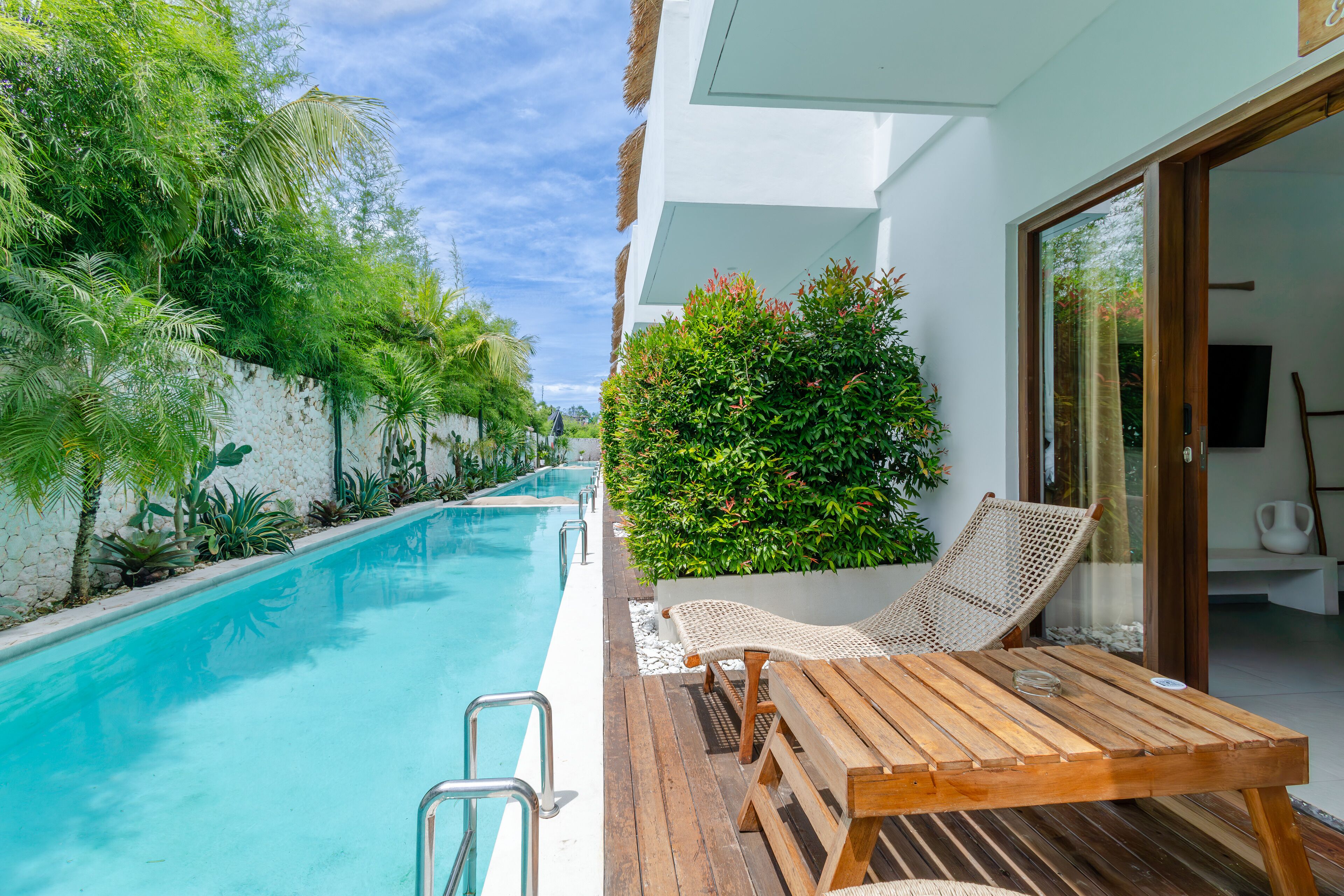 A poolside area with a wooden deck, lounge chairs, and a glass door leading to a room.