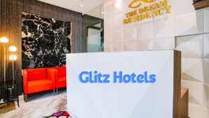 A hotel reception area with a marble wall, a red sofa, and a sign for 'Glitz Hotels'. - Glitz Hotels DR Residency (Mumbai)