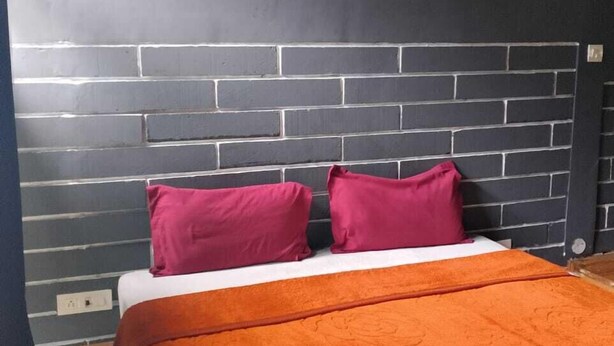 A bedroom with a brick-patterned headboard, a bed with an orange bedspread, and two pink pillows. - Crestwood Kasauli Heights (Kasauli)