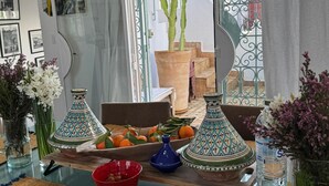 Un coin repas avec une table dressée pour deux personnes, agrémenté d’un cactus, d’oranges et de vases décoratifs.