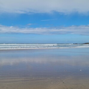 Una playa con olas, cielo despejado y roquedos distantes.