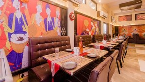 A restaurant with long communal tables, brown leather booths, and colorful murals on the walls. - Pheonix By Glitz Hotels (Panvel)
