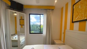 A bedroom with a bed, a mirror, a TV, and a window with curtains. - Magical Sunsets at Coco Sunset Hills (Playas del coco)