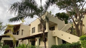 A multi-story building with a sloped roof, surrounded by lush greenery and palm trees. - Magical Sunsets at Coco Sunset Hills (Playas del coco)