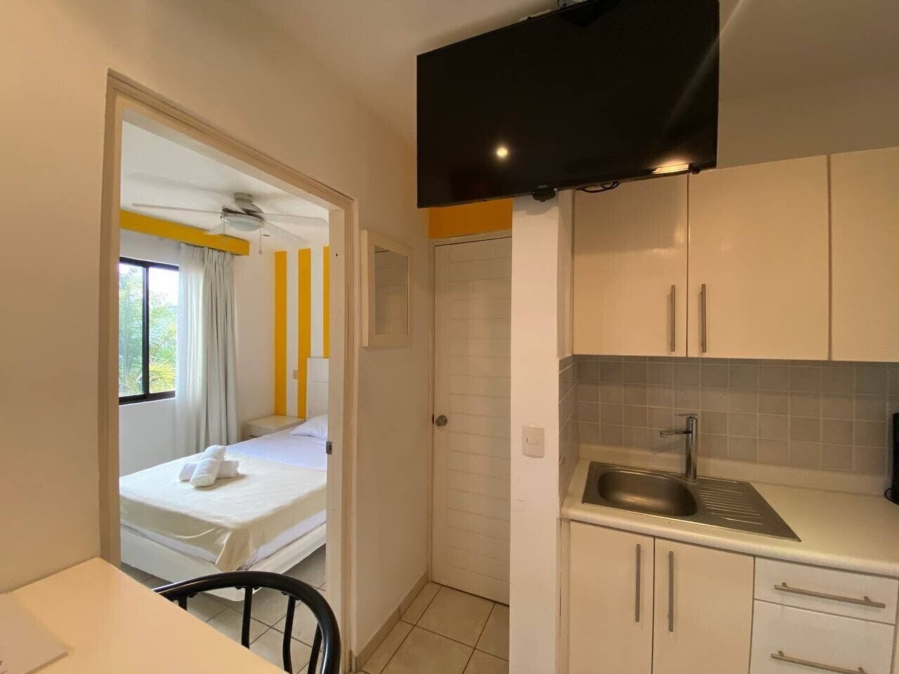 A compact hotel room with a bed, a small kitchenette, and a bathroom.