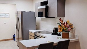 A compact kitchen with a refrigerator, microwave, stove, and a small dining area with two chairs. - Brand New Condo - Heart of Coco! (Coco)