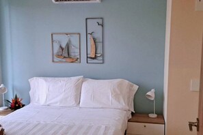 A bedroom with a bed, two wall-mounted paintings, bedside lamps, and a nightstand.