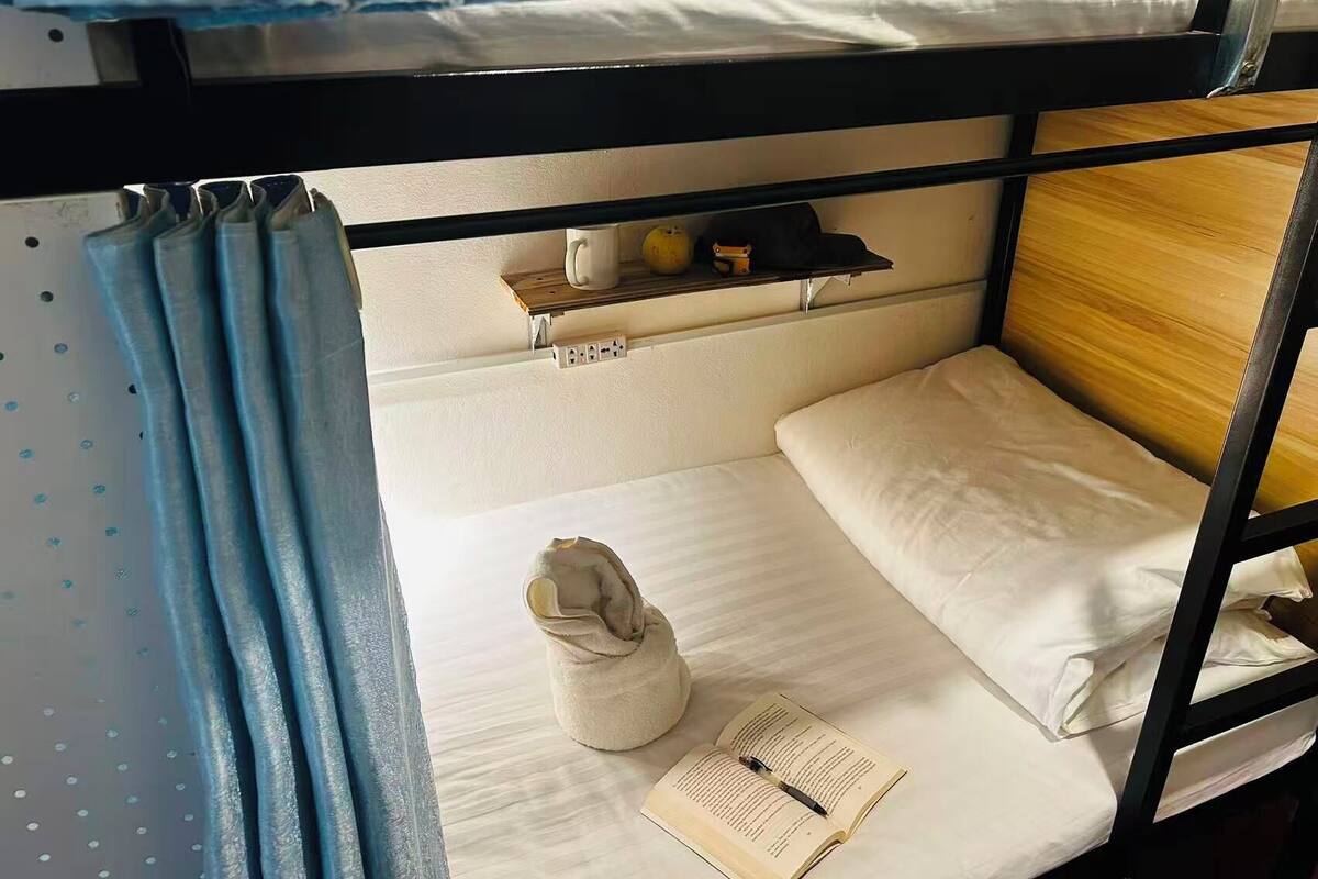 A bunk bed room with a shelf above the lower bunk, a towel, and an open book on the lower bed.