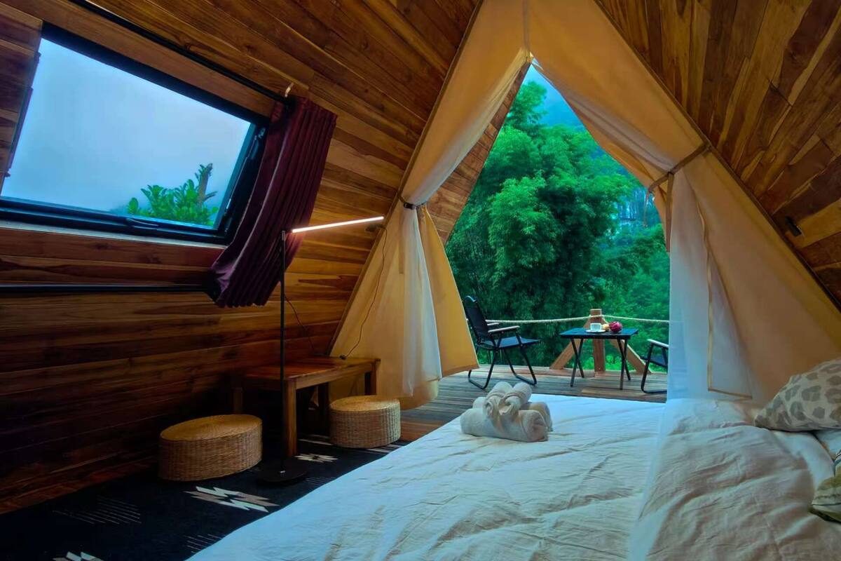 A cozy, wooden tent-style room with a bed, a window, and a view of a lush green forest.