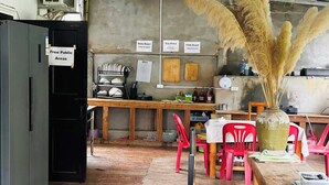 A rustic interior with a wooden counter, red plastic chairs, a vase with pampas grass, and signs indicating 'Free Public Areas' and 'Done-Board.'