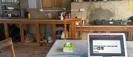 A rustic kitchen with wooden countertops, a laptop on a table, and signs indicating different areas for food preparation.