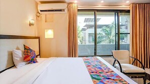 A hotel room with a bed, a chair, a window with curtains, and an air conditioning unit. - PS By Glitz Hotels (Navi Mumbai)