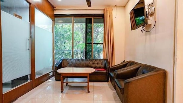A room with a sofa, a table, and a TV mounted on the wall. - PS By Glitz Hotels (Navi Mumbai)