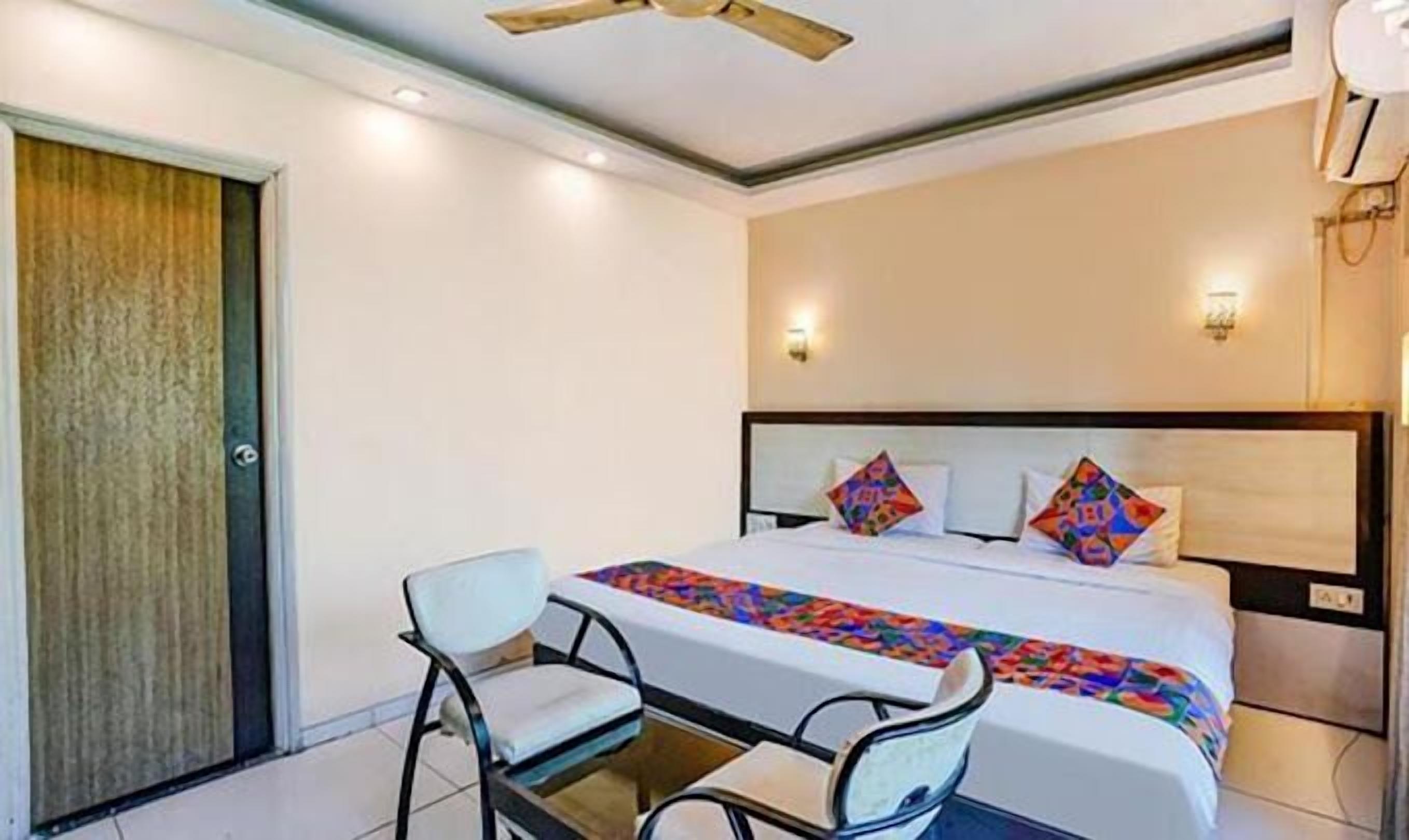 A hotel room with a bed, two chairs, a ceiling fan, and a door.
