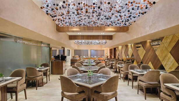 A spacious dining area with multiple tables and chairs, a decorative ceiling, and a modern interior design. - The Fern Residency Ahmedabad, Ellisbridge, Series by Marriott (Ahmedabad)