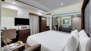 A hotel room with a bed, a desk with a flat-screen TV, a dining area with plates of food, and a bathroom visible through a glass door. - The Fern Residency Ahmedabad, Ellisbridge, Series by Marriott (Ahmedabad)