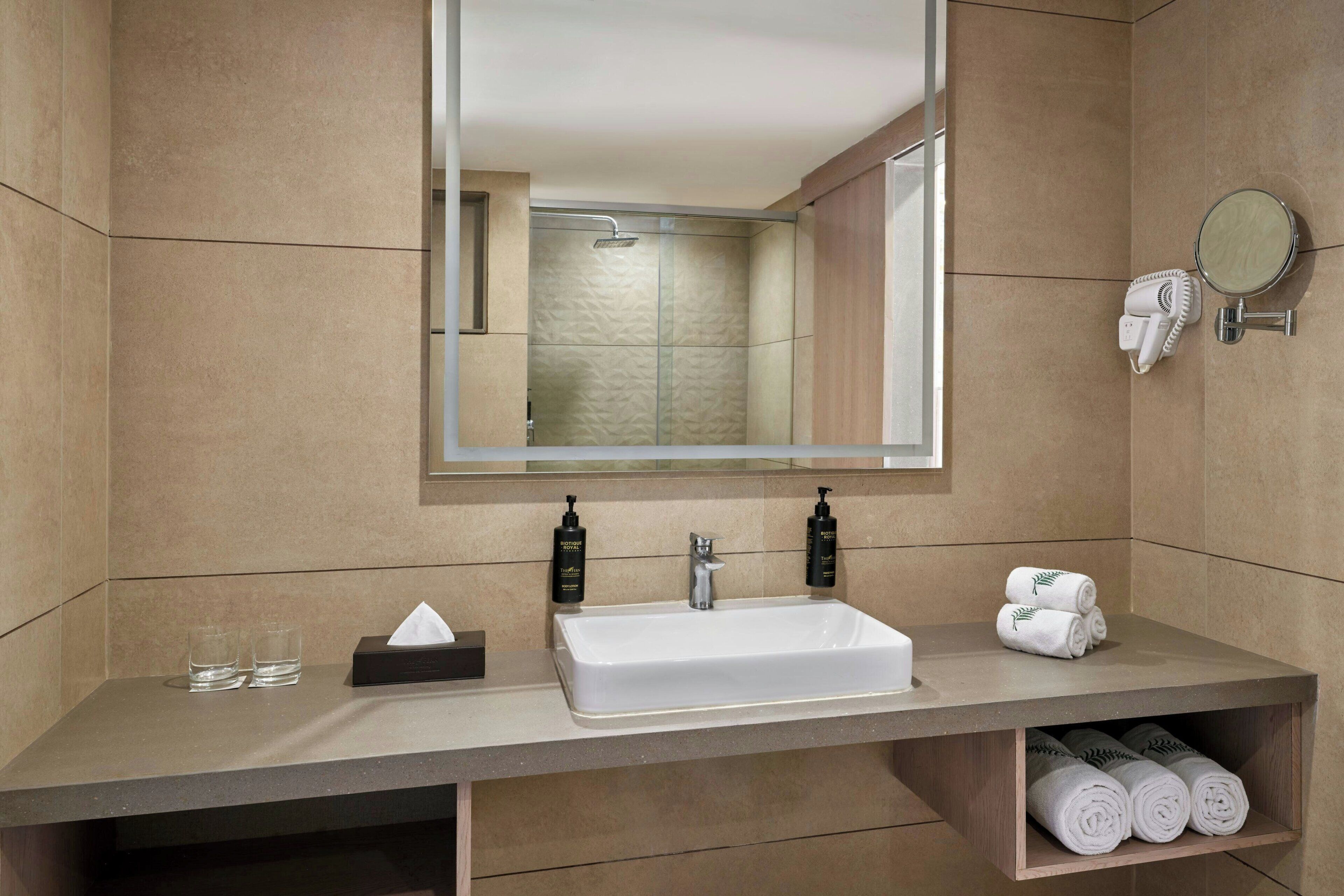 A bathroom with a large mirror, a sink, two bottles of shampoo, a towel rack, and a shelf with towels.
