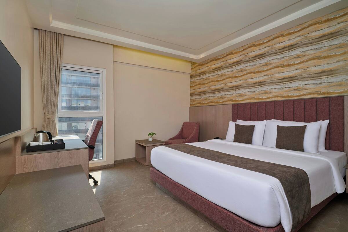 A hotel room with a bed, desk, chair, and a window with curtains.