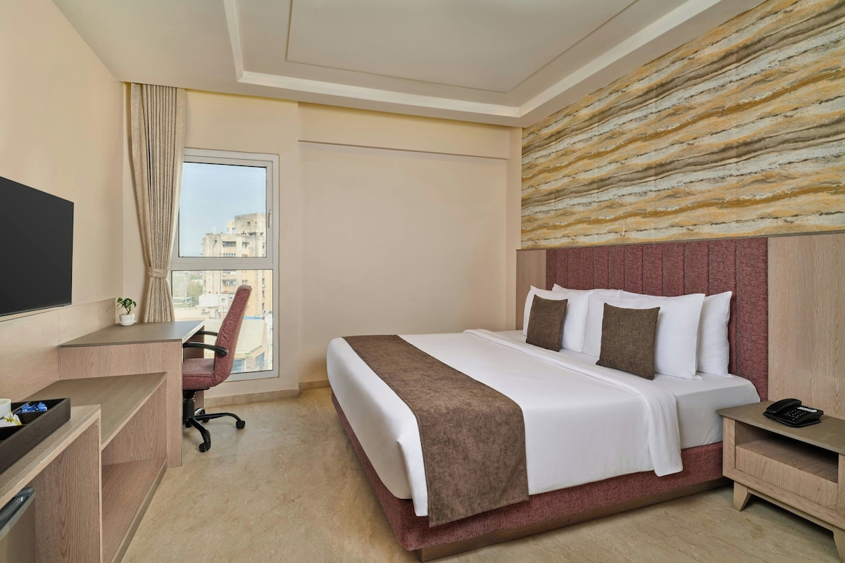 Una habitación de hotel con cama, escritorio, silla y un ventanal grande.
