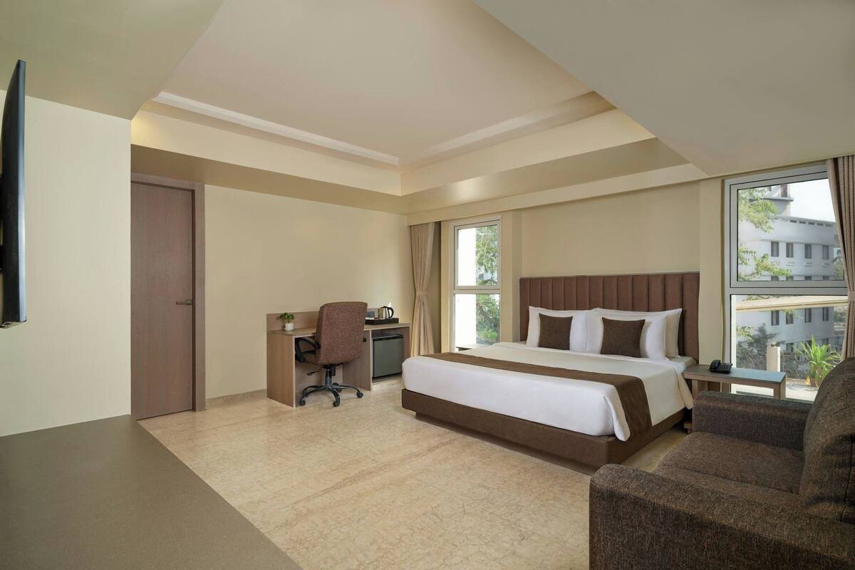 A hotel room with a bed, desk, chair, and a view of the outside.