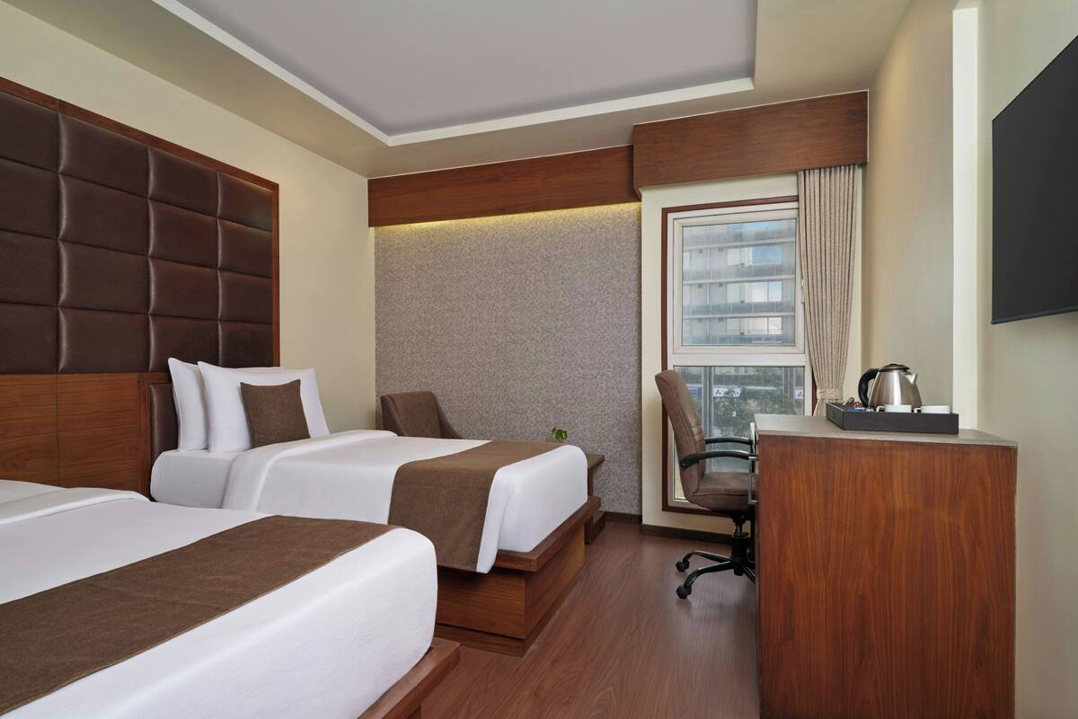 A hotel room with two beds, a desk, a chair, and a television.